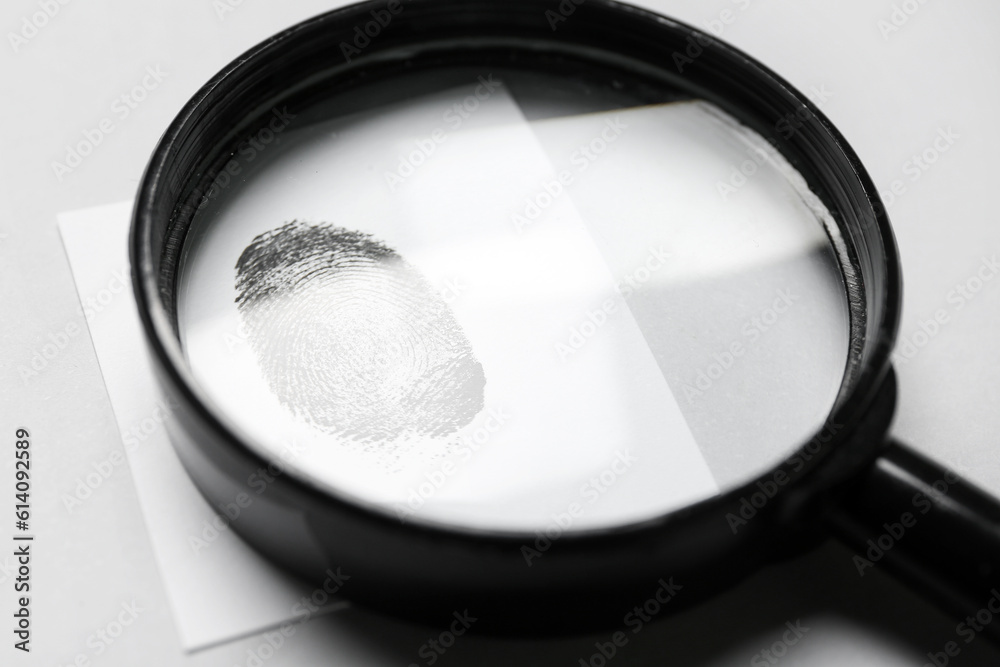 Magnifier and paper with fingerprint on grey background. Detective concept