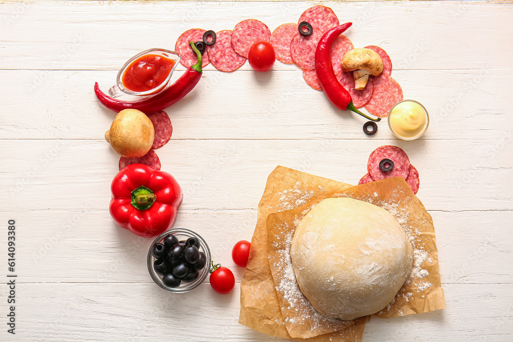 Frame made of raw dough and ingredients for preparing pizza on light wooden background