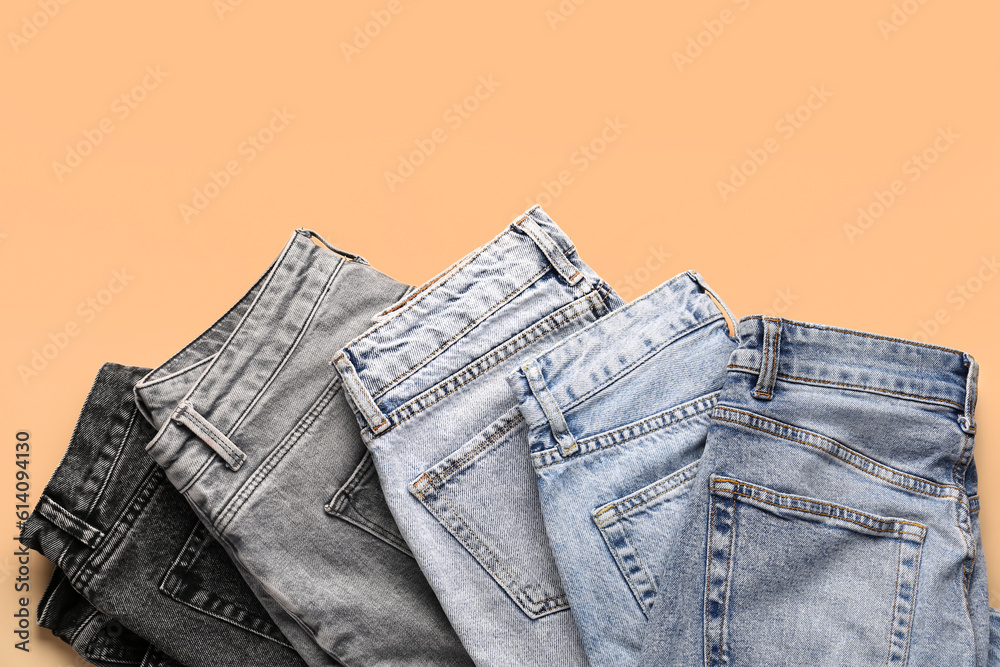 Different stylish folded jeans on pale orange background