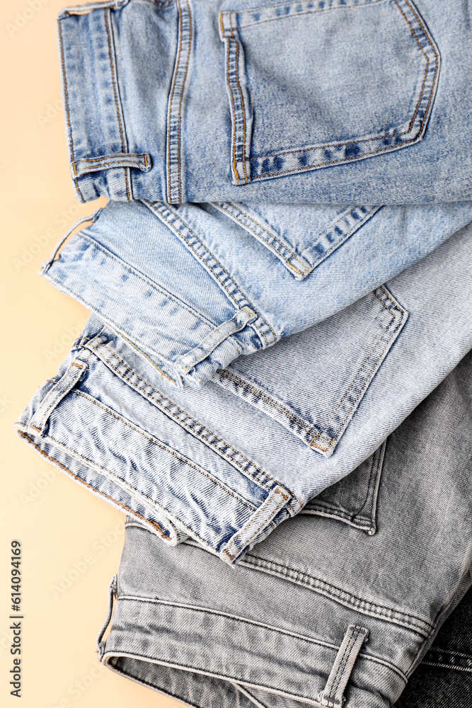 Different stylish folded jeans on pale orange background