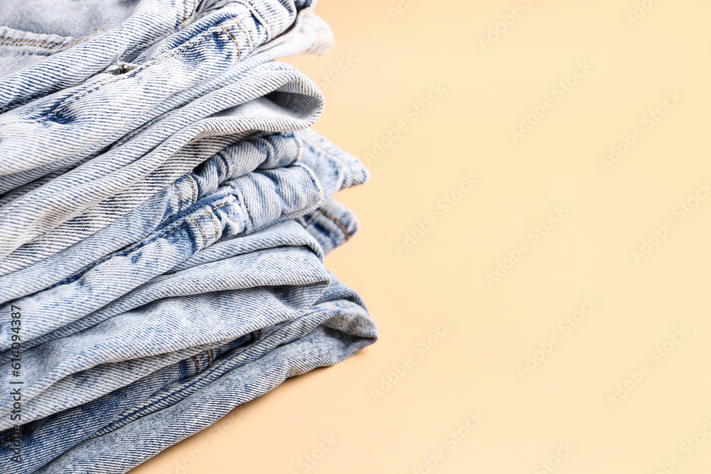 Stack of different stylish jeans on pale orange background