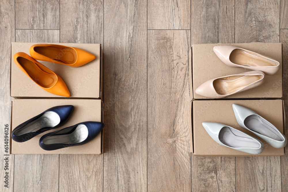 Cardboard boxes with stylish high-heeled shoes on light wooden background