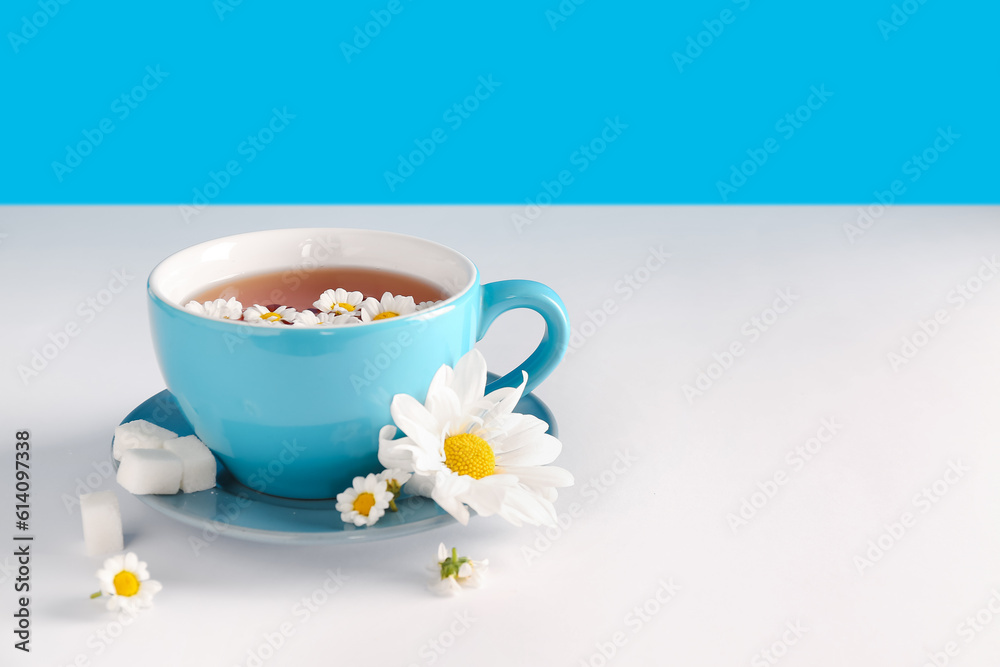 Cup of natural chamomile tea and flowers on white table near blue wall