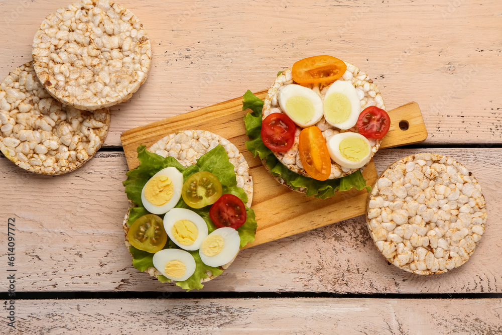 Rice crackers with quail eggs, tomatoes and lettuce on light wooden background