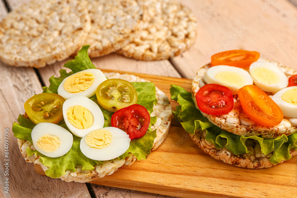 Rice crackers with quail eggs, tomatoes and lettuce on light wooden background, closeup