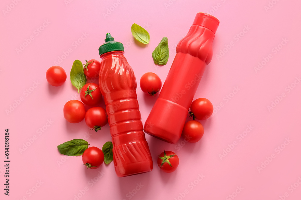 Bottles of ketchup and tomatoes on pink background