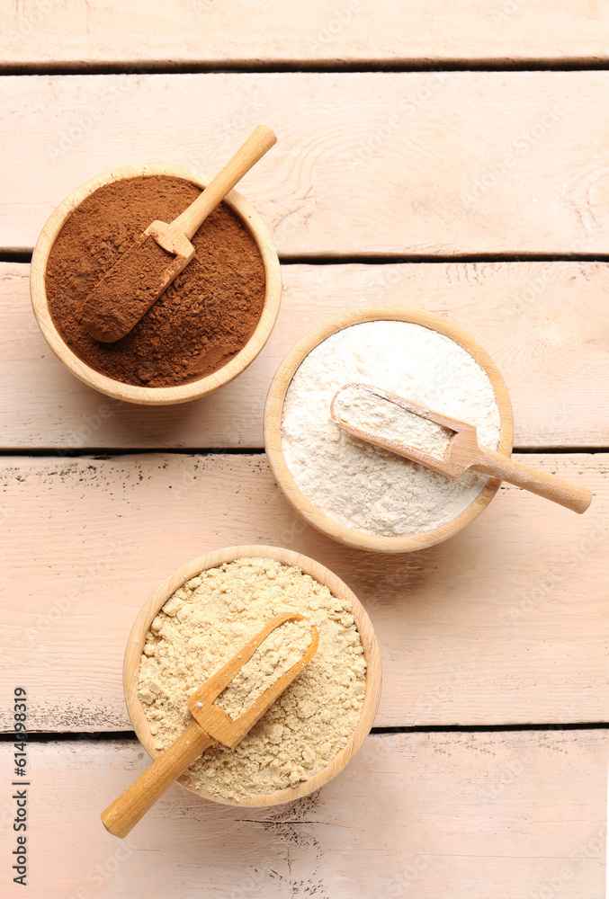 Wooden bowls with different types of flour and cacao on light wooden background