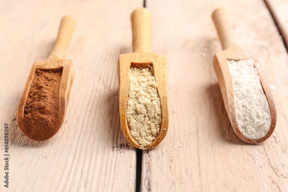 Wooden scoops with different types of flour and cacao on light wooden background