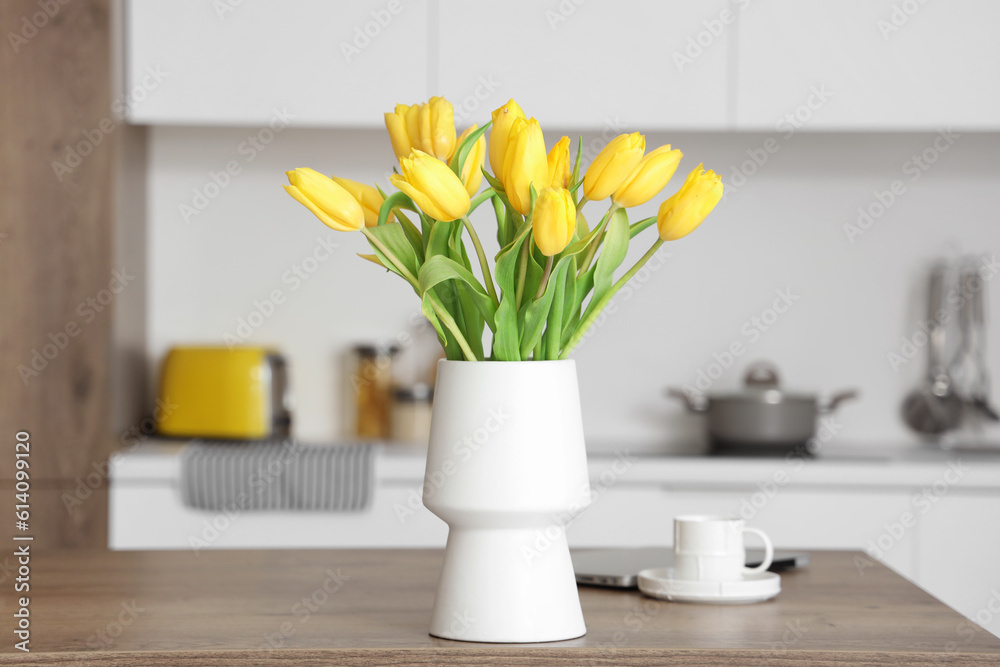 Vase with yellow tulip flowers on wooden table in modern kitchen