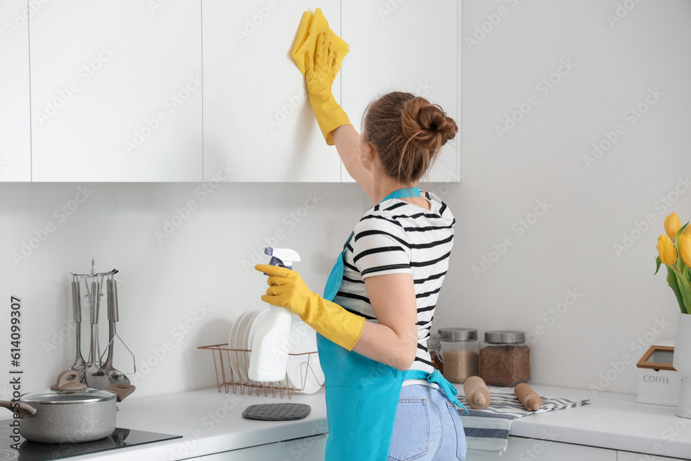 Woman in yellow rubber gloves cleaning cupboards in modern kitchen