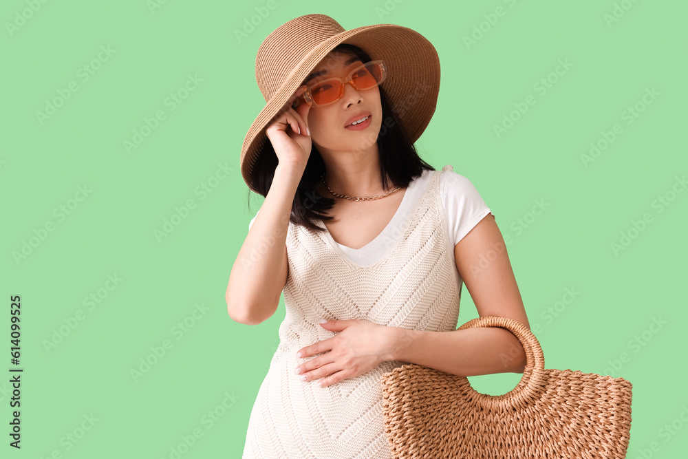 Beautiful Asian woman in stylish sunglasses with bag on green background