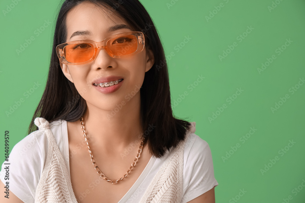 Beautiful Asian woman in stylish sunglasses on green background, closeup