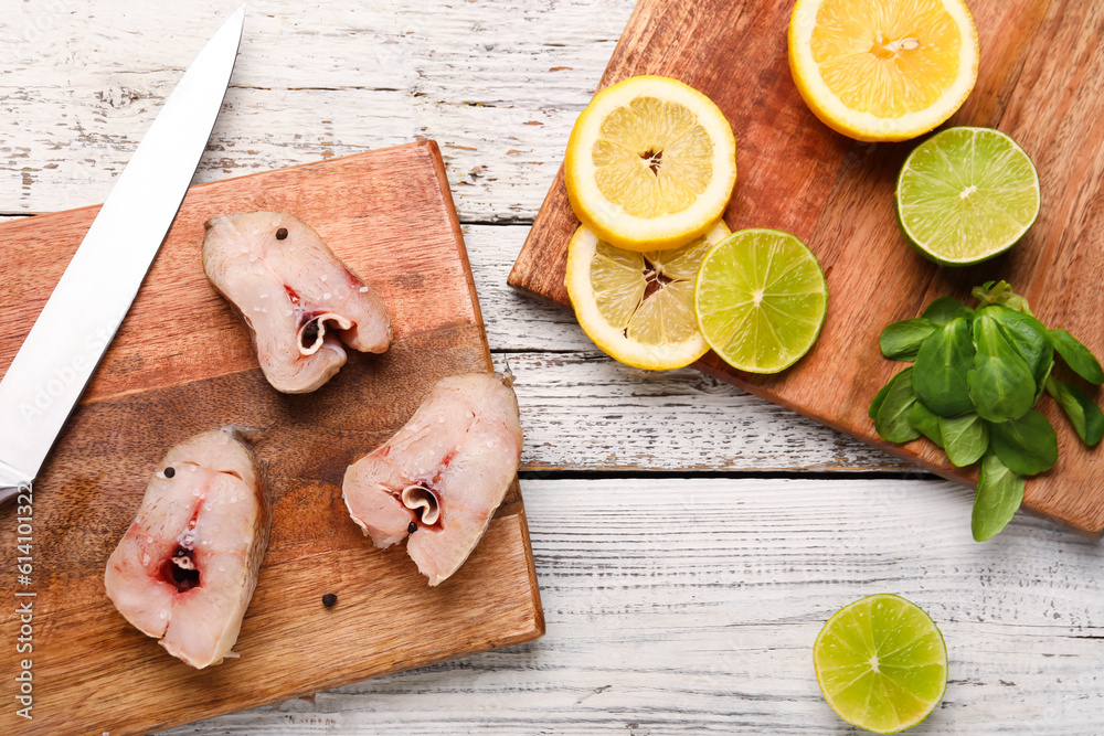 Boards with pieces of raw codfish, lime and lemon on light wooden background