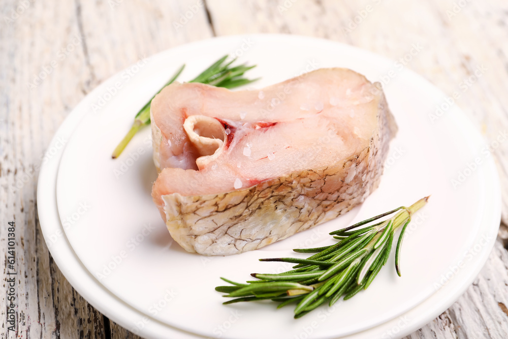 Plate with piece of raw codfish on light wooden background