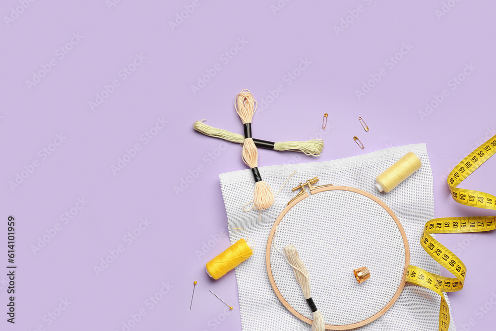 Embroidery hoop with canvas, mouline threads and measuring tape on lilac background