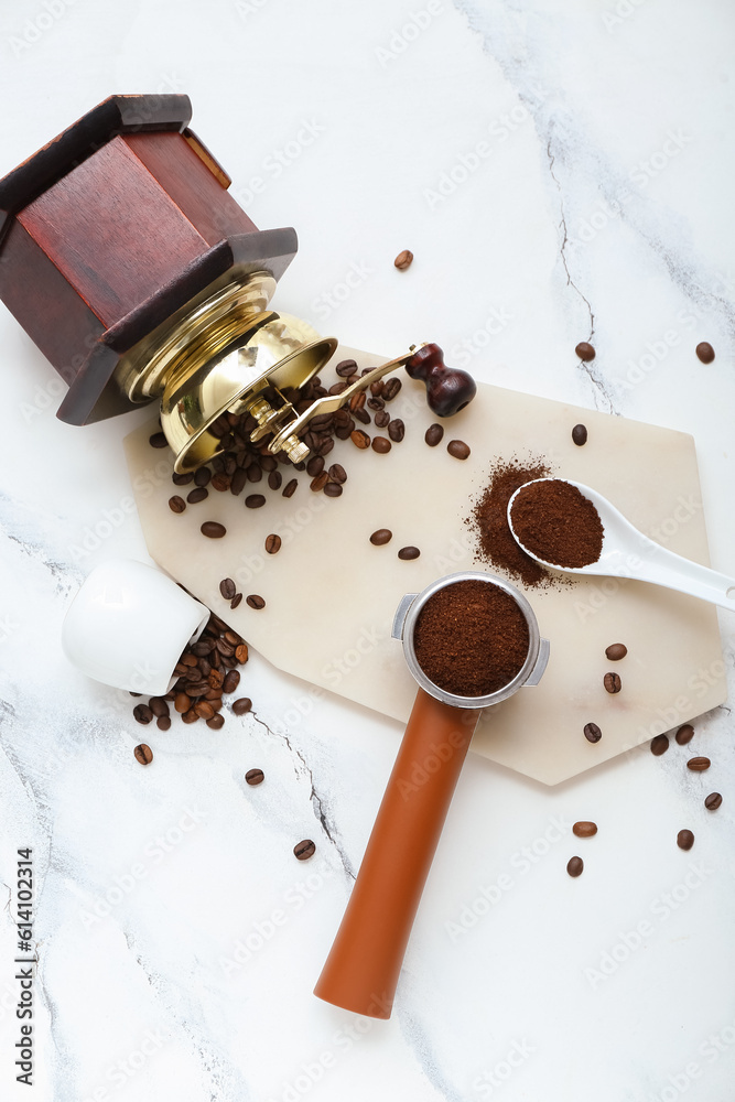 Portafilter with coffee grinder, powder and beans on white marble background