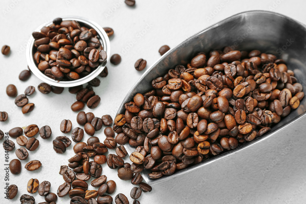 Scoop and bowl with coffee beans on light background