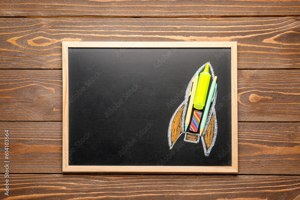 Drawn rocket with marker, pens and eraser on chalkboard on wooden background