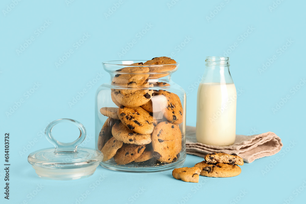 Jar with cookies, bottle of milk and towel on blue background