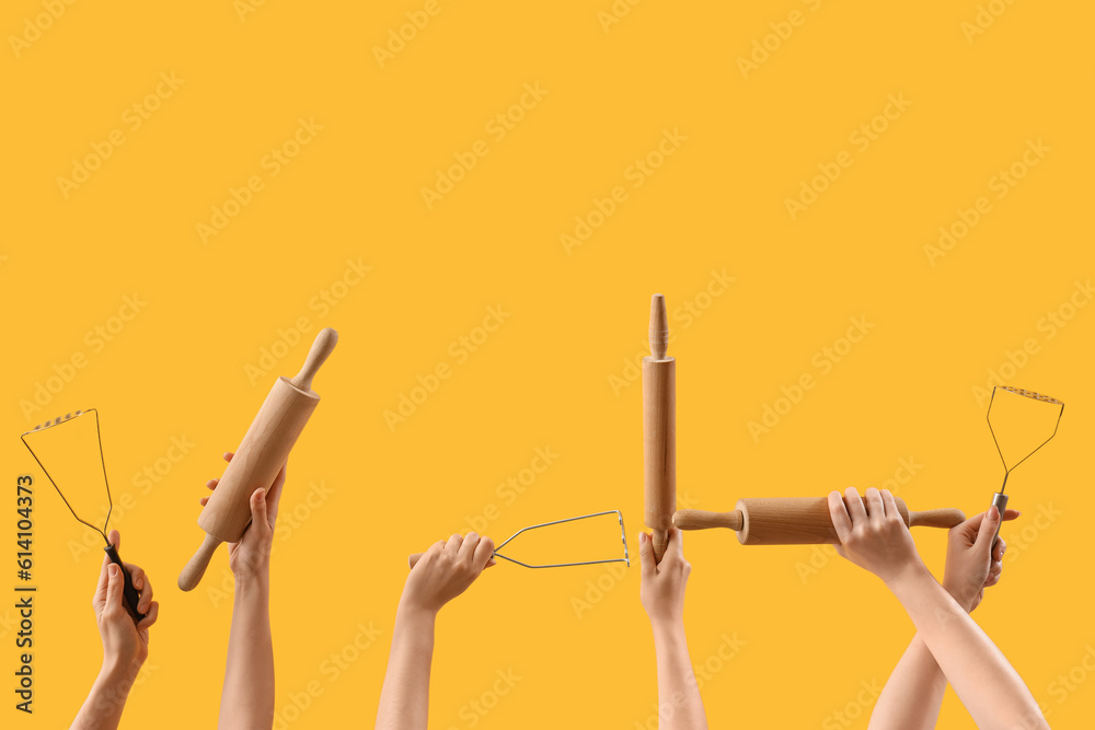 Female hands holding rolling pins and mashers on yellow background