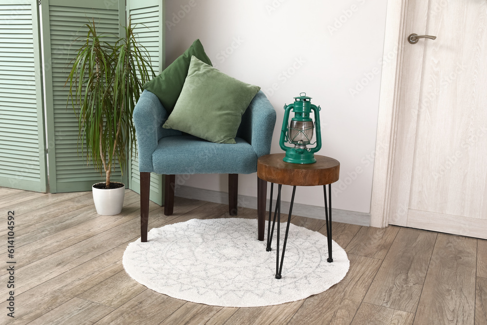 Interior of living room with blue armchair, folding screen, houseplant and stool