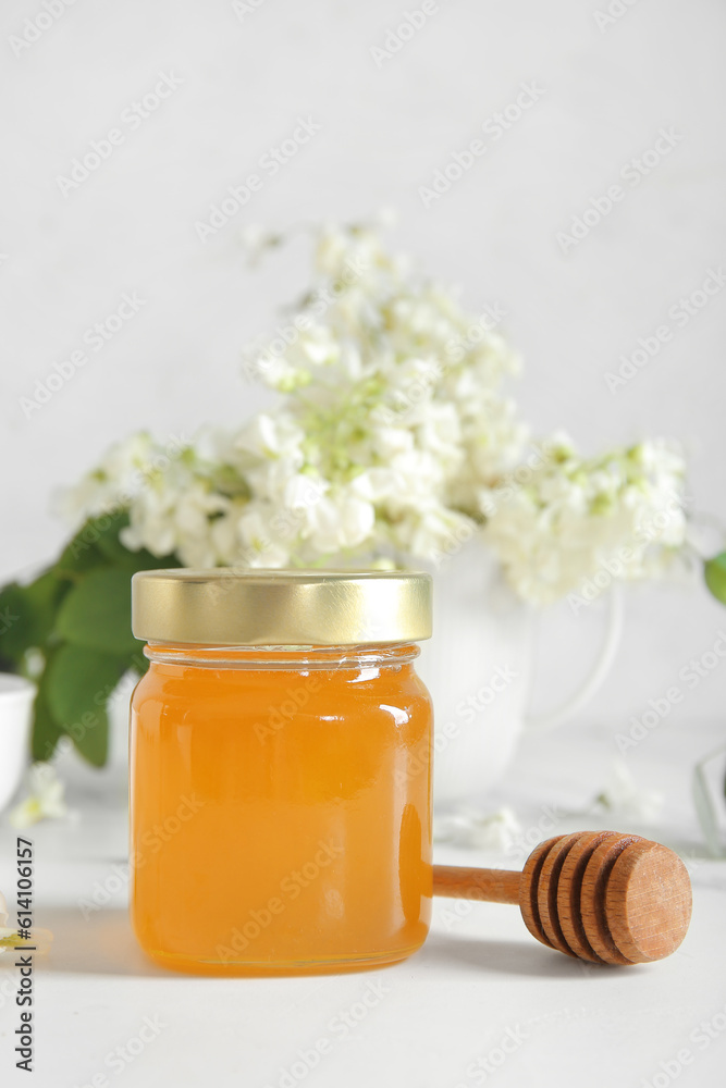 Jar of honey with flowers of acacia and dipper on light background, closeup