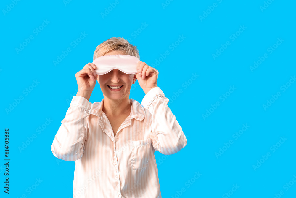 Mature woman in pajamas with sleeping mask on blue background