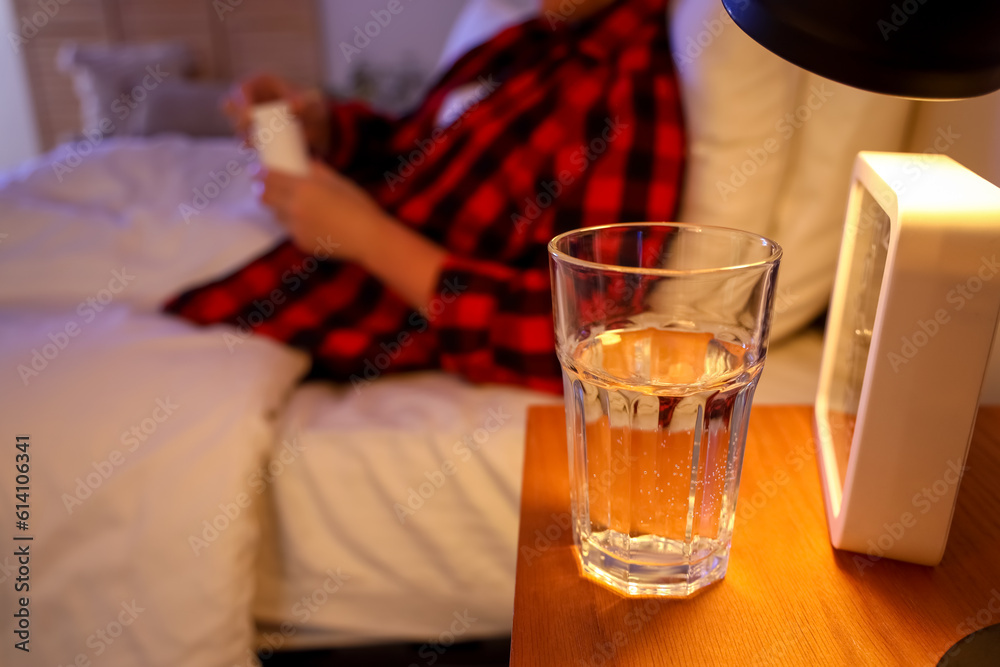 Glass of water and clock on table in bedroom of mature woman at night, closeup