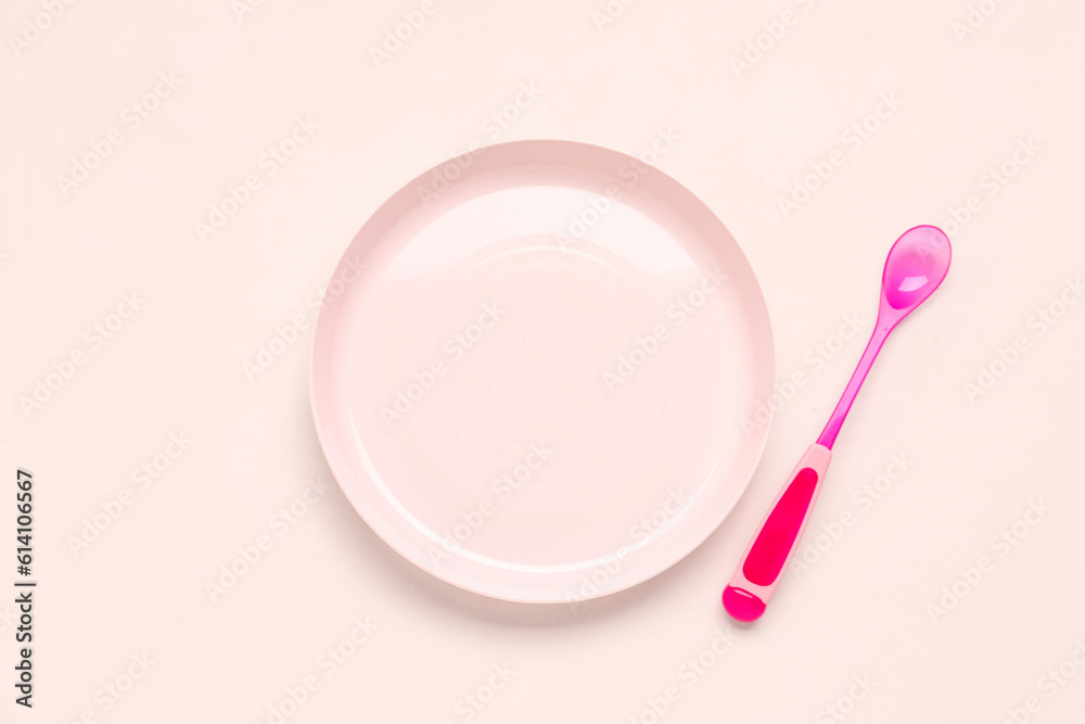 Plate with spoon for baby on pink background