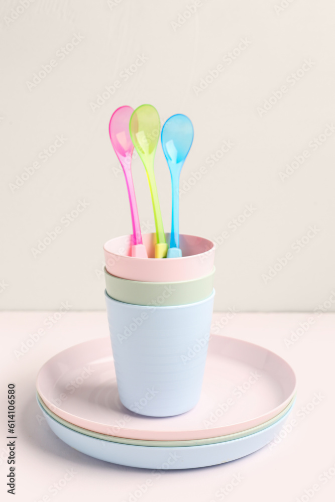 Plates with spoons and cups for baby on white table