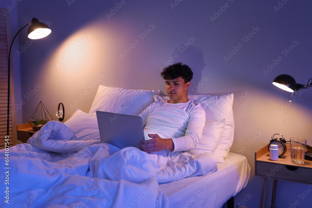 Young man using laptop in bed at night