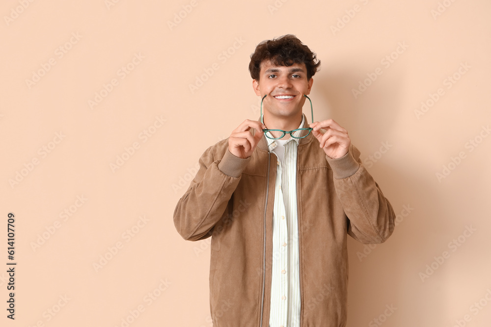 Young man with stylish eyeglasses on beige background