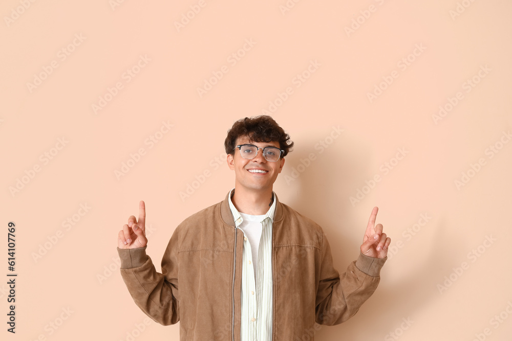 Young man in stylish eyeglasses pointing at something on beige background