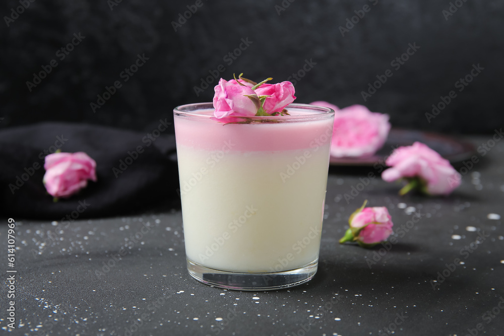 Glass of panna cotta with beautiful pink rose flowers on black table