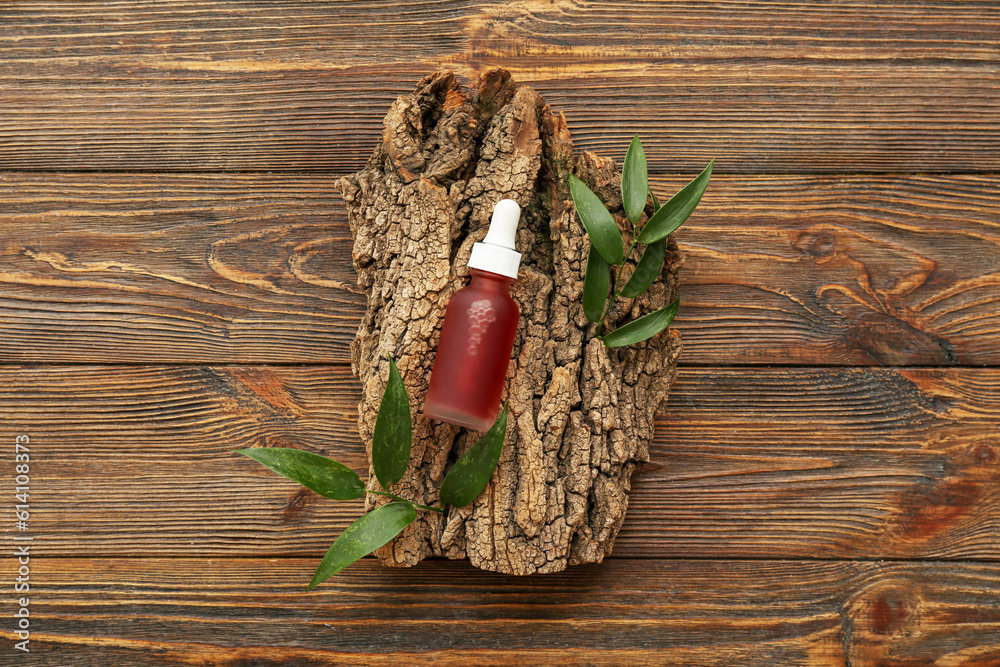 Composition with bottle of essential oil, tree bark and plant leaves on wooden background