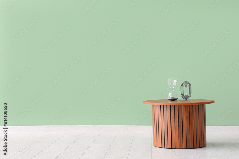 Wooden coffee table with hourglass and decorative figure near green wall