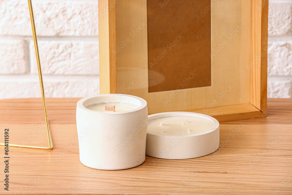 Holders with candles and frame on table near light brick wall in room, closeup