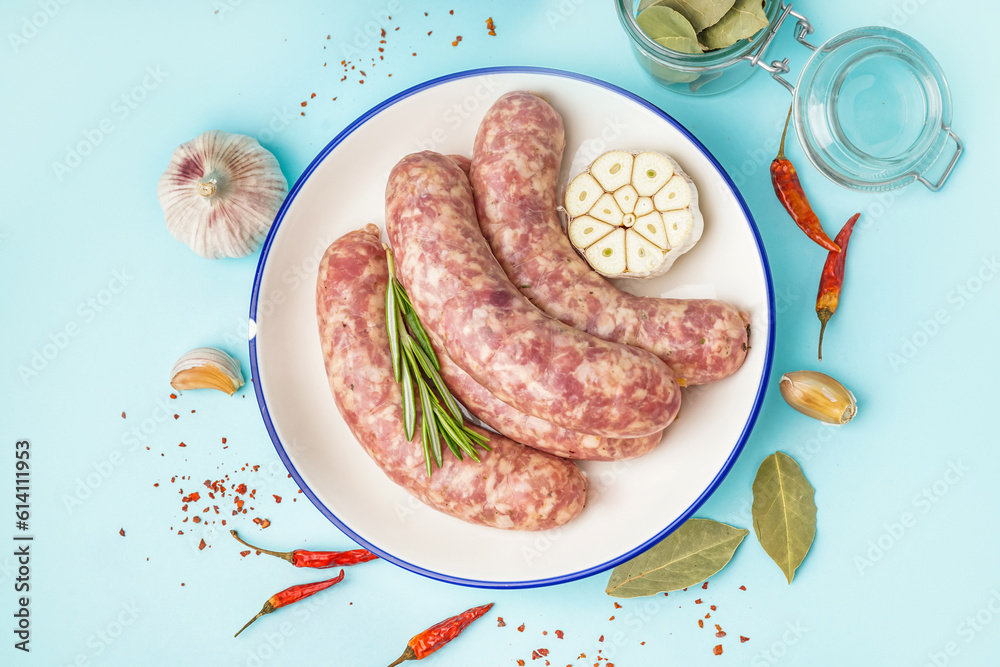 Plate with raw fresh sausages and spices on blue background