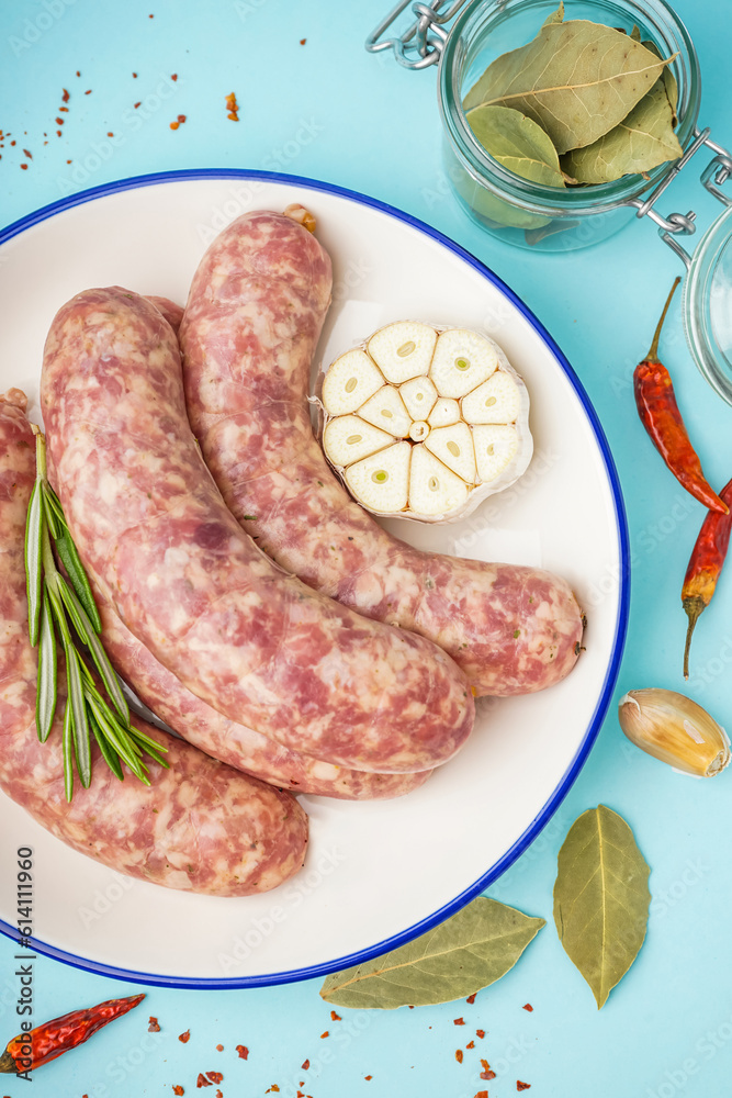 Plate with raw fresh sausages and spices on blue background