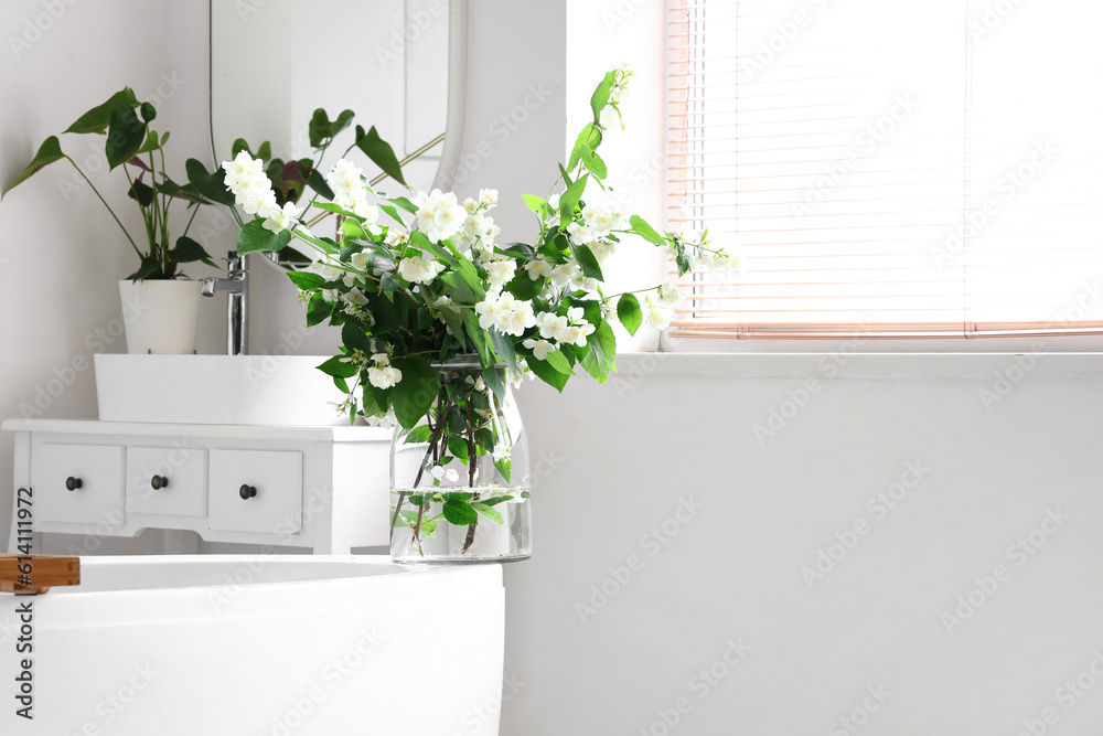 Vase with blooming jasmine flowers on bathtub in interior of light bathroom