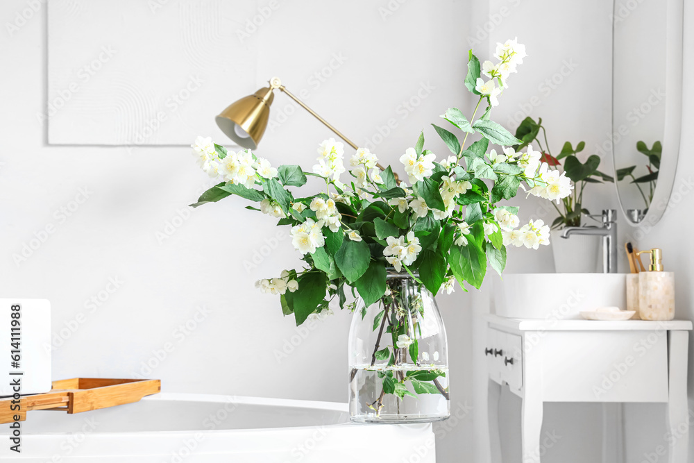 Vase with blooming jasmine flowers on bathtub in interior of light bathroom