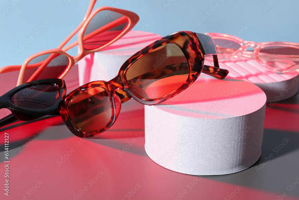 Podiums with different stylish sunglasses on colorful background