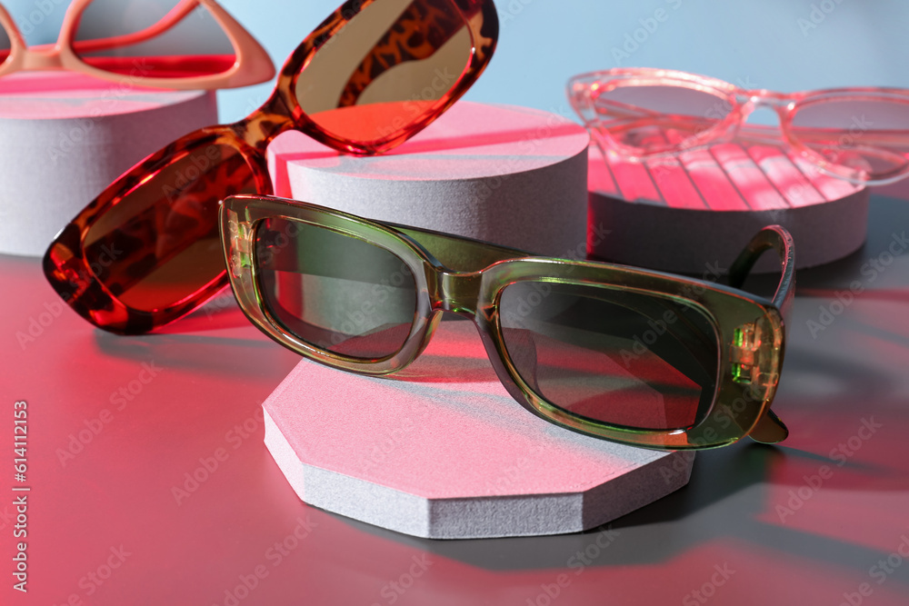 Podiums with different stylish sunglasses on colorful background