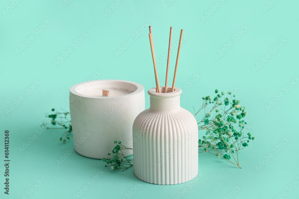 Floral reed diffuser with candle and gypsophila flowers on turquoise background