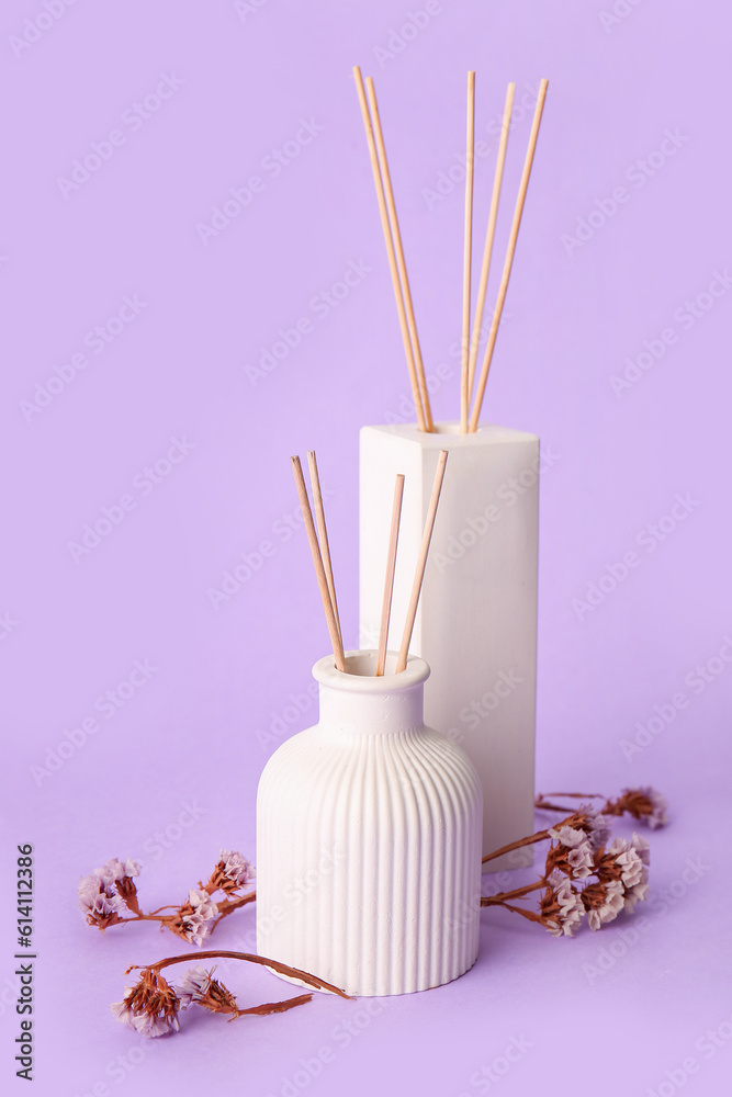 Bottles of reed diffuser and flowers on purple background