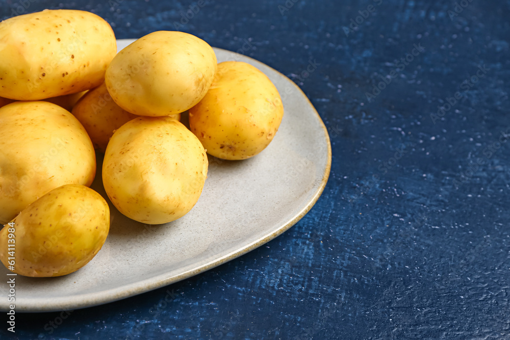 Plate with raw baby potatoes on blue background