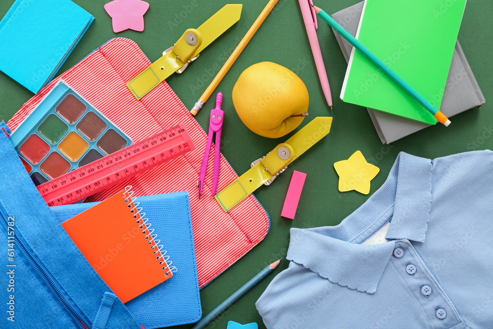 Backpack with shirt, apple and different stationery on green background