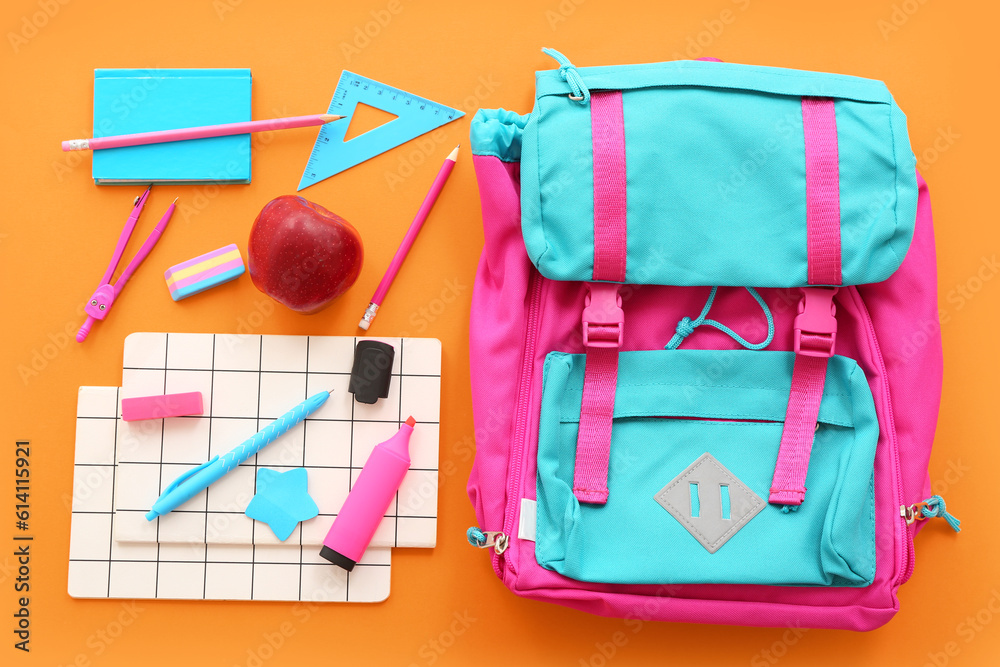 Backpack with fresh red apple and different stationery on orange background