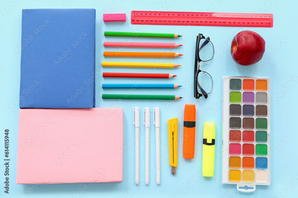 Eyeglasses with fresh red apple and different stationery on blue background