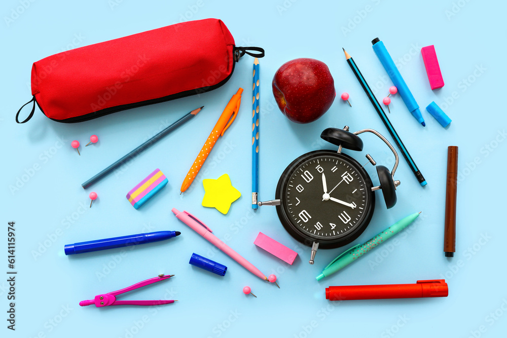 Alarm clock with fresh apple, pencil case and different stationery on blue background